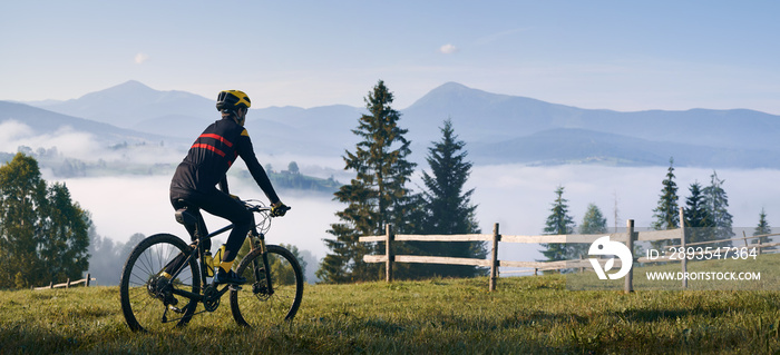 男子骑自行车在长满草的小山上，看着美丽的薄雾山。男子骑自行车享受