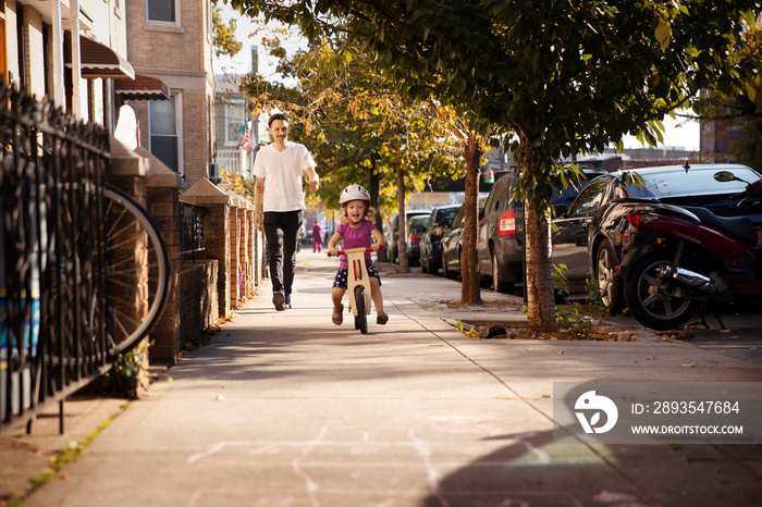 Small girl (2-3) riding on bicycle with father