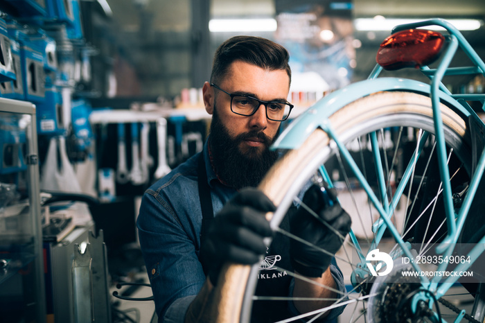 Young beard bicycle mechanic repairing bicycles in a workshop..