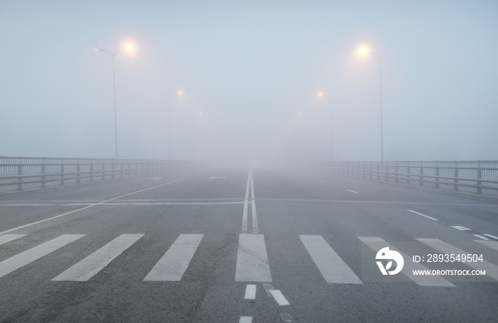 浓雾中一条空荡荡的柏油路（高速公路）。人行道、十字路口、街道照明