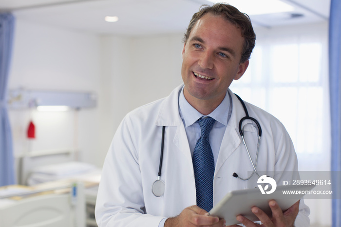 Portrait smiling male doctor with digital tablet making rounds in hospital