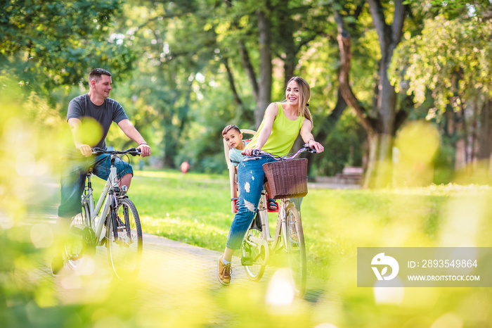 快乐的父亲和母亲带着孩子骑着自行车在公园里玩得很开心。快乐的家庭……