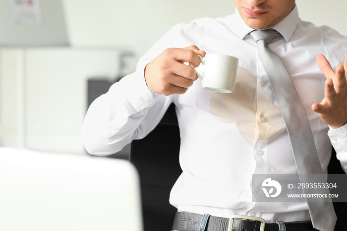 Stressed young businessman with coffee stains on his shirt in office