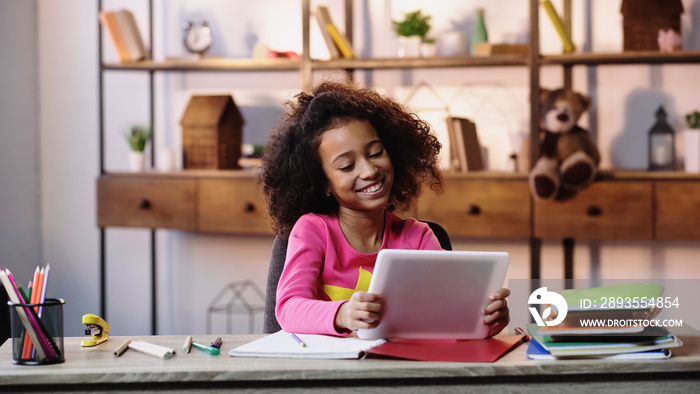 cheerful african american girl using digital tablet near notebooks on desk.