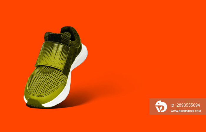 Yellow sports shoe for children on a orange, lush lava background. The concept of using sport shoes 