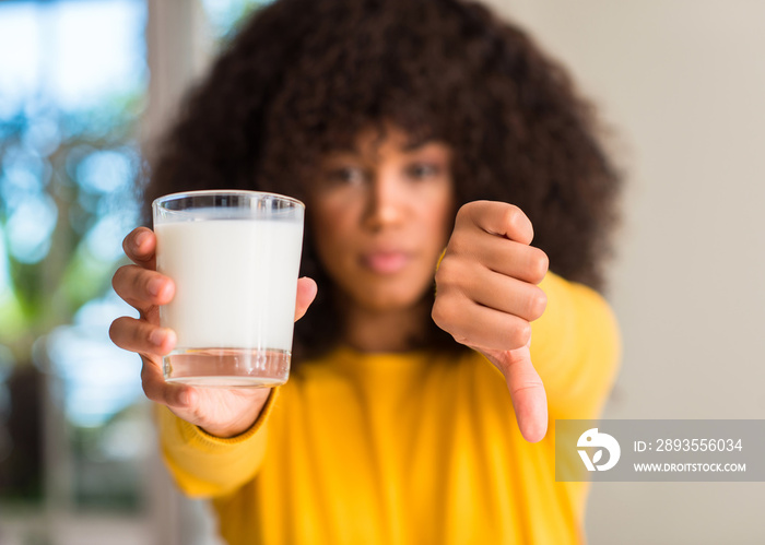 African american woman holding a glass of milk with angry face, negative sign showing dislike with t