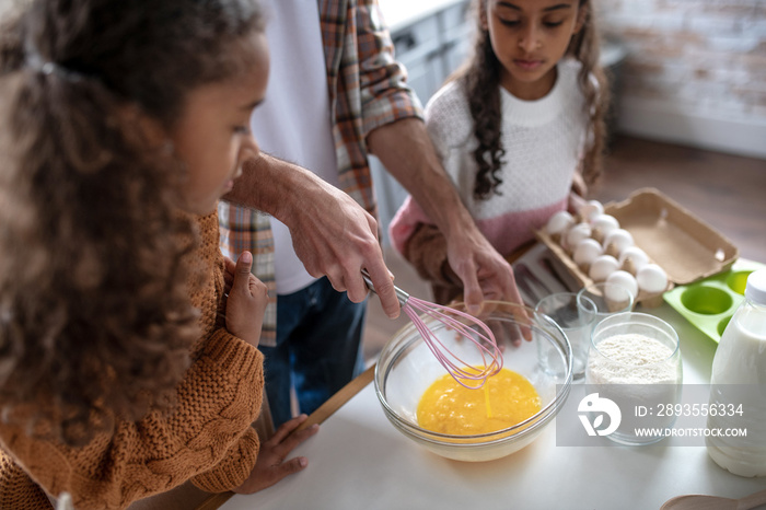 Girls watching their father whipping eggs while cooking pie