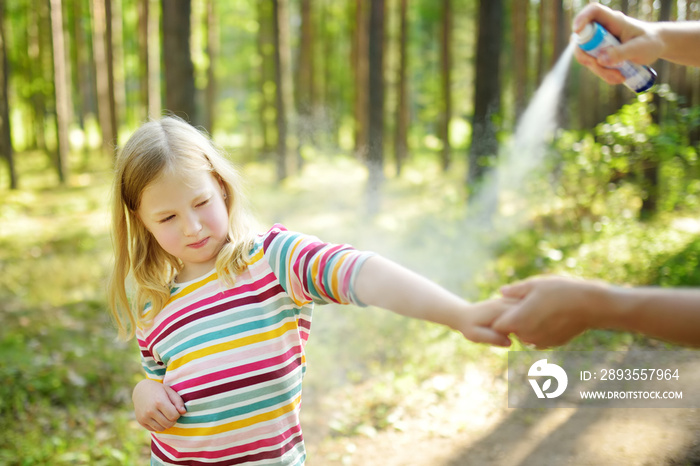 Mother applying insect repellent to her daughter before forest hike summer day. Protecting children 