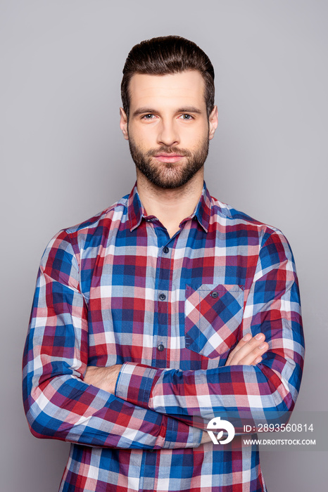 A portrait of young confident man in checkered shirt with crossed arms isolated on gray background