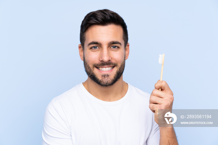 Young handsome man with beard brushing his teeth over isolated background smiling a lot