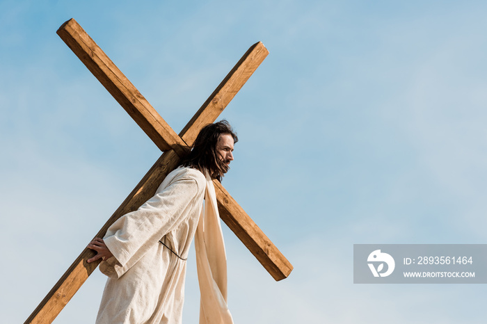 bearded jesus holding wooden cross against sky