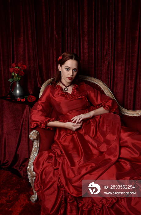 portrait of pretty female model with red hair wearing glamorous historical victorian red ballgown.  