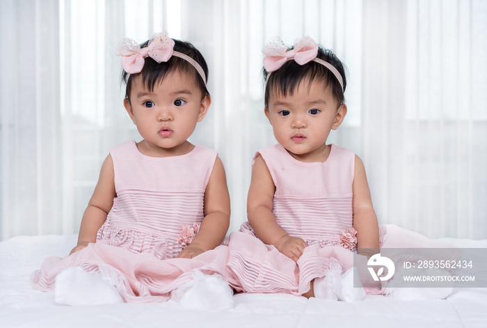 床上两个穿着粉色连衣裙的双胞胎婴儿