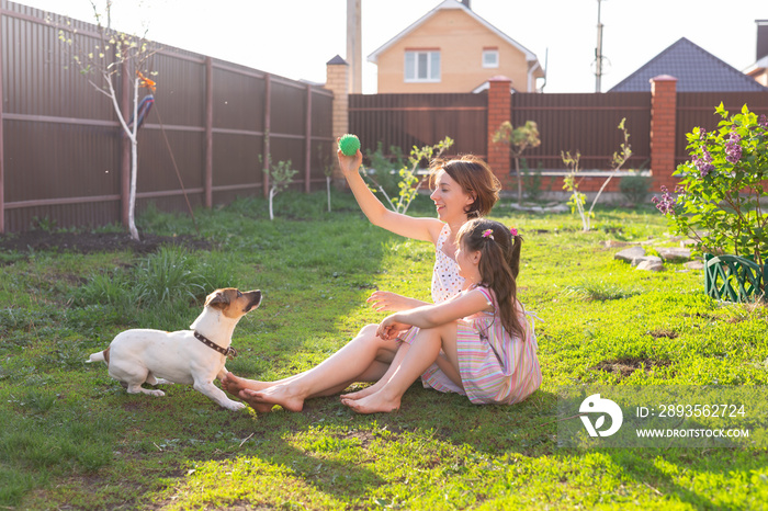Little girl in pink dress with mother and jack russell terrier dog laying on grass.