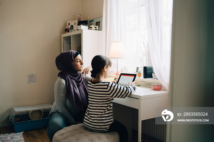 Mother assisting daughter in homework through digital tablet at bedroom