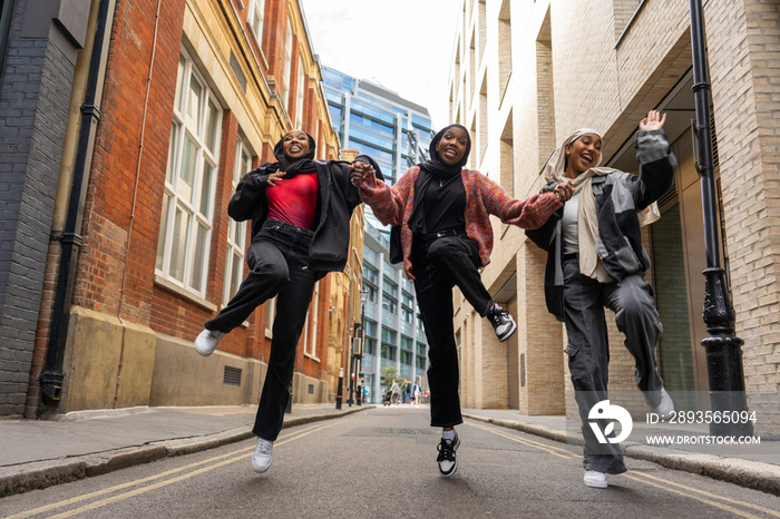 Three young women wearing�hijabs�holding hands and jumping in city