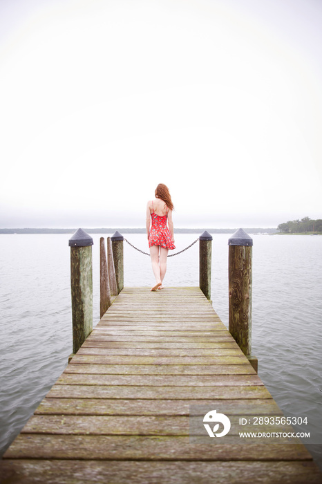 Woman in floral dress standing on pier looking at lake