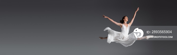 身着白色连衣裙的优雅女人在灰色的横幅上独自跳跃