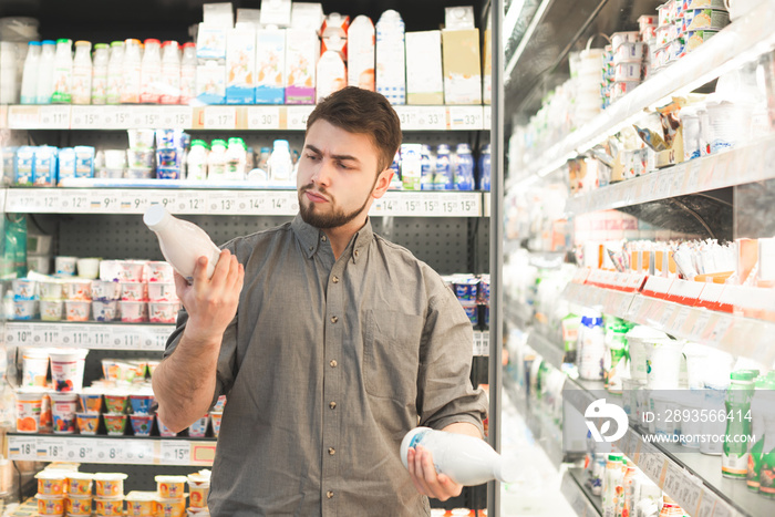 Portrait of a man with a beard selects yogurt bottle in a supermarket,looks at labels and reads the 