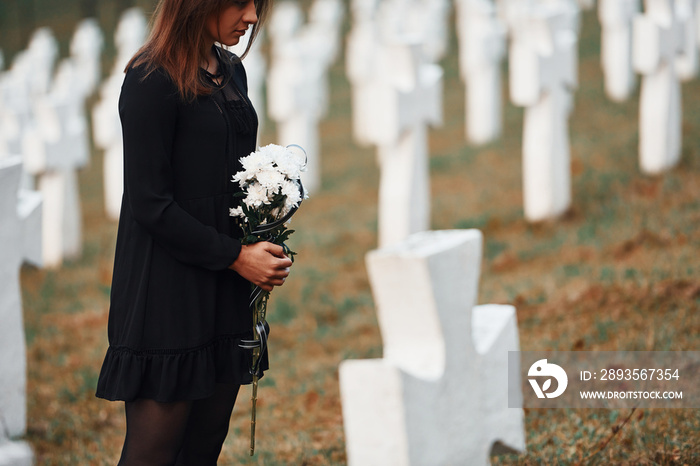 粒子视图。身穿黑衣的年轻女子带着许多白色十字架参观墓地。概念