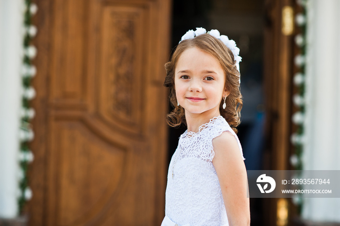 Portrait of cute little girl on white dress and wreath on first