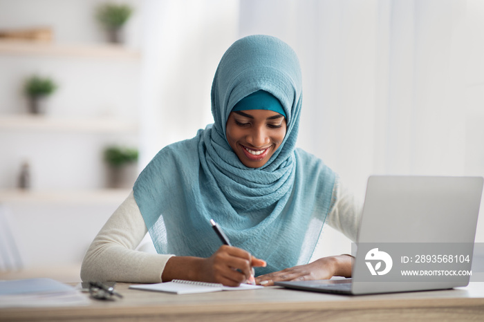远程学习概念。带着笔记本电脑在Hijab学习中微笑的黑人伊斯兰妇女