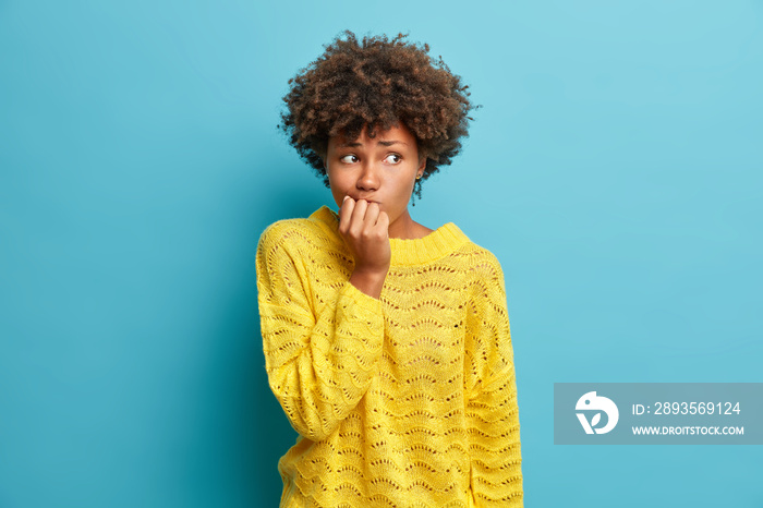 Portrait of nervous Afro American woman keeps hands near mouth feels concerned before important inte