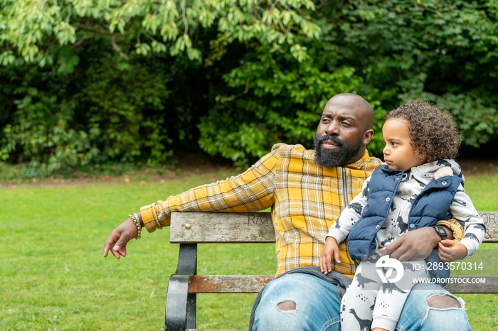 Man with daughter on laps sitting on bench in park