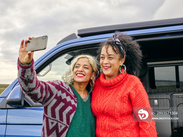 Female couple taking selfie in front of van