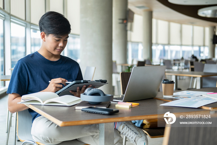 Young collage student using computer and mobile device studying online.