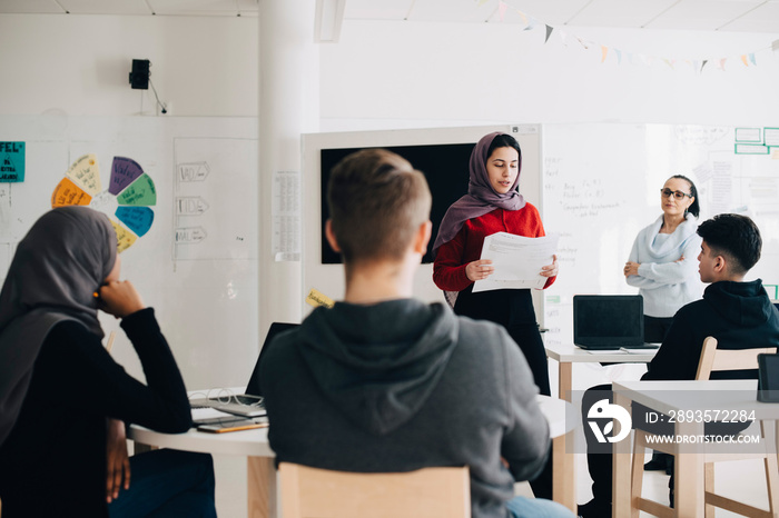 Teacher looking at student giving presentation in university classroom