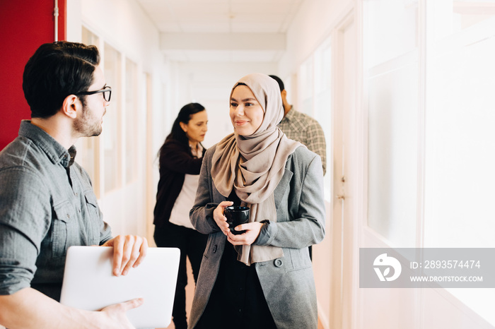 Multi-ethnic colleagues discussing while standing in corridor at office