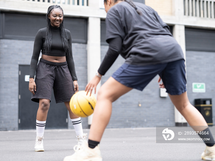 Two female friends playing basketball outdoors