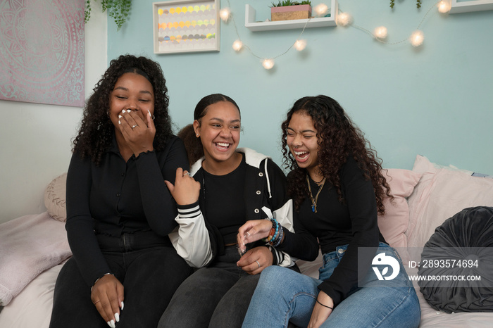 Laughing teenage friends sitting on bed in bedroom