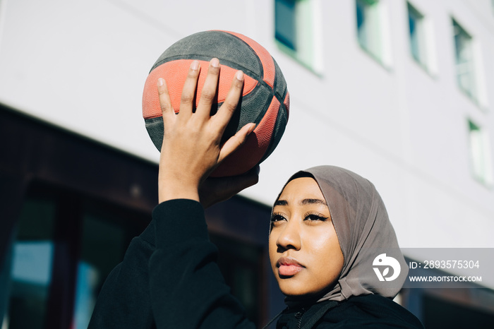 Close-up of teenage girl wearing hijab playing with ball at schoolyard during sunny day