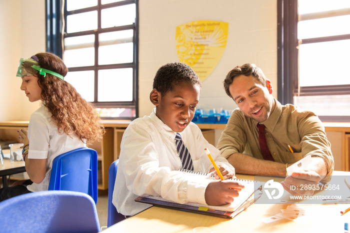 Portrait of male teacher demonstrating scientific sample and schoolboy (8-9) sitting at desk writing