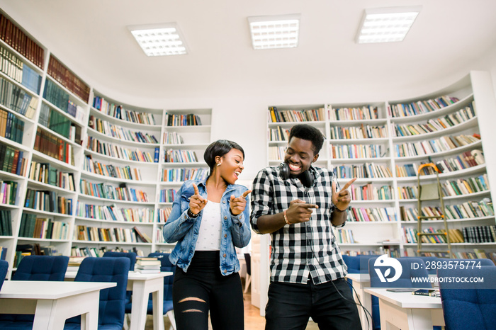 Beautiful African-American cheerful couple of students have a fun and dancing in the library. The gi