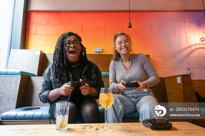 Female friends having fun while playing in video games at pub