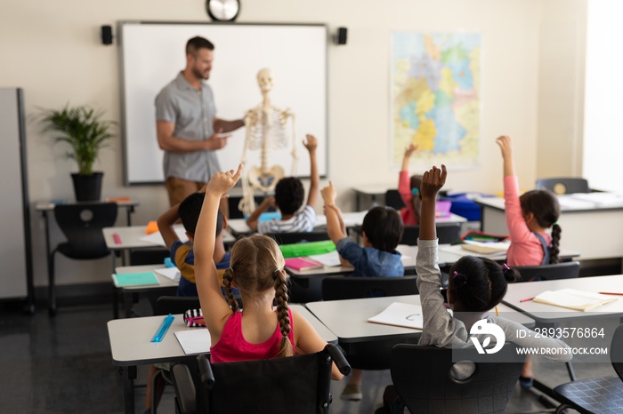 School kids raising hand and sitting at desk in elementary