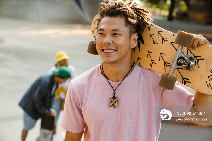 Asian boy smiling and holding skateboard at skate park