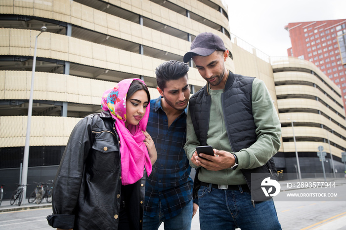 Three friends in standing in street, looking at smartphone