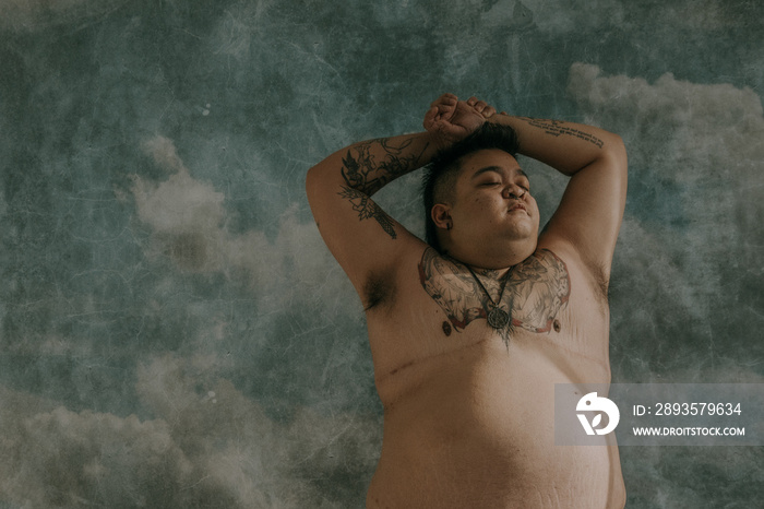 portrait of a plus size trans-masculine person with hands over head looking towards the sun