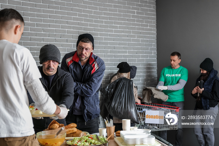 Volunteers giving food and clothes to homeless people in warming center