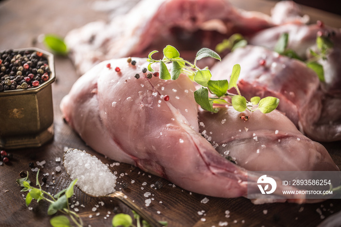 Raw rabbit legs salt pepper and herbs on butcher board