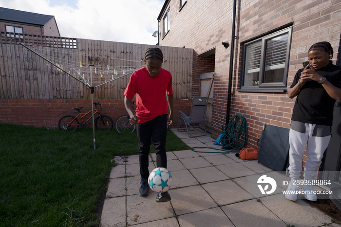 Teenage boy?photographing friend playing soccer in back yard