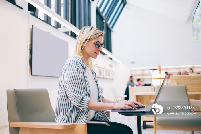 Serious young female student typing on laptop in library