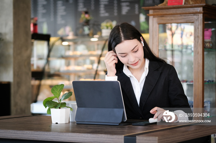 Businesswoman in formal suit wearing wireless earphone and working with tablet computer at modern ca