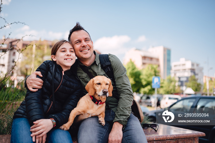 Father and daughter resting on a city street with their dog