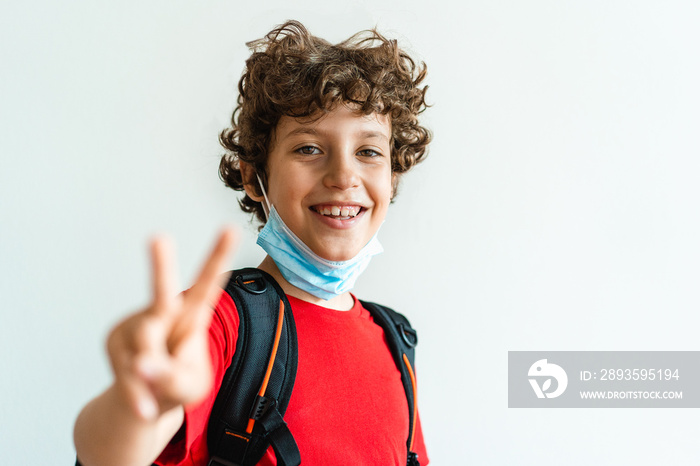 Little guy with backpack and pulled down safety mask making the V Victory sing with his fingers. Lif