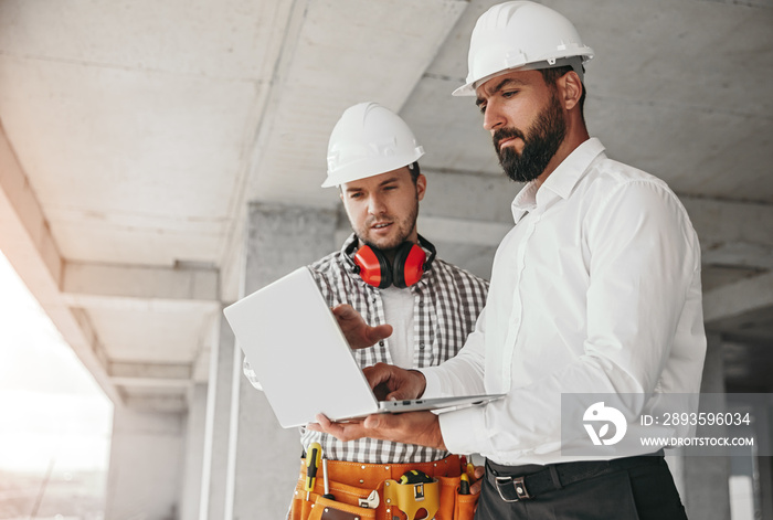 Male contractors using laptop on construction site